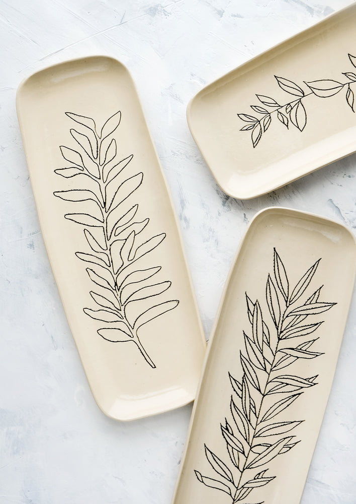 Tall and slender ceramic platters in natural bisque color with etched black botanical drawings