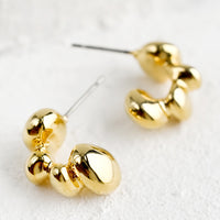 2: A pair of gold hoop earrings in melty blob shape.