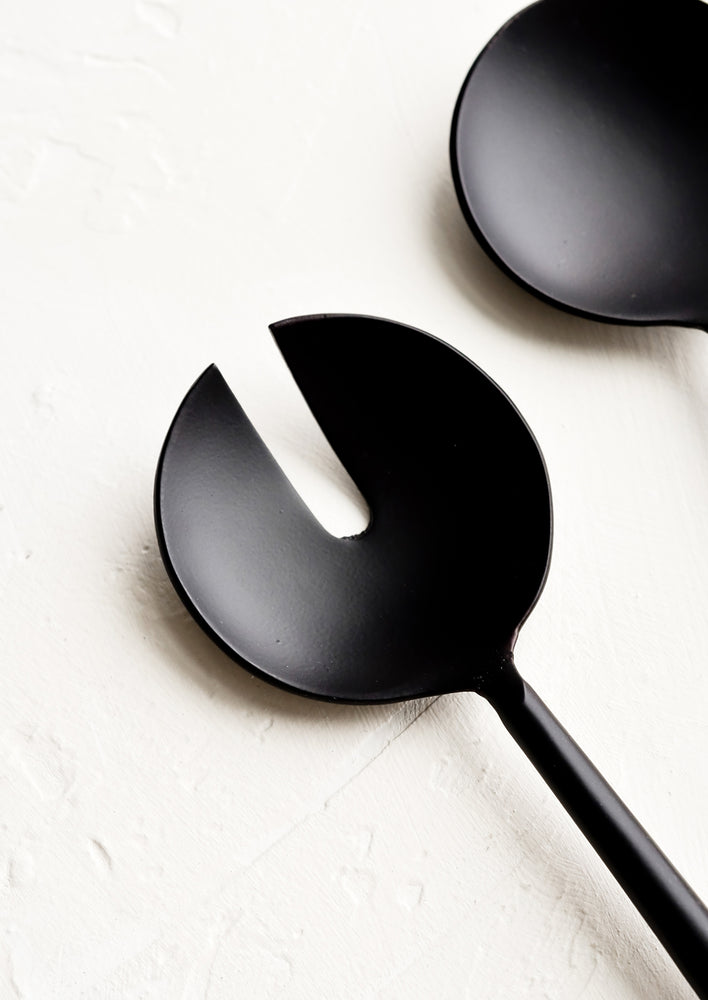 2: A round, matte black metal serving spoon with a slotted notch in the center.