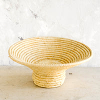 3: Footed pedestal bowl made from natural woven raffia, sitting on a table