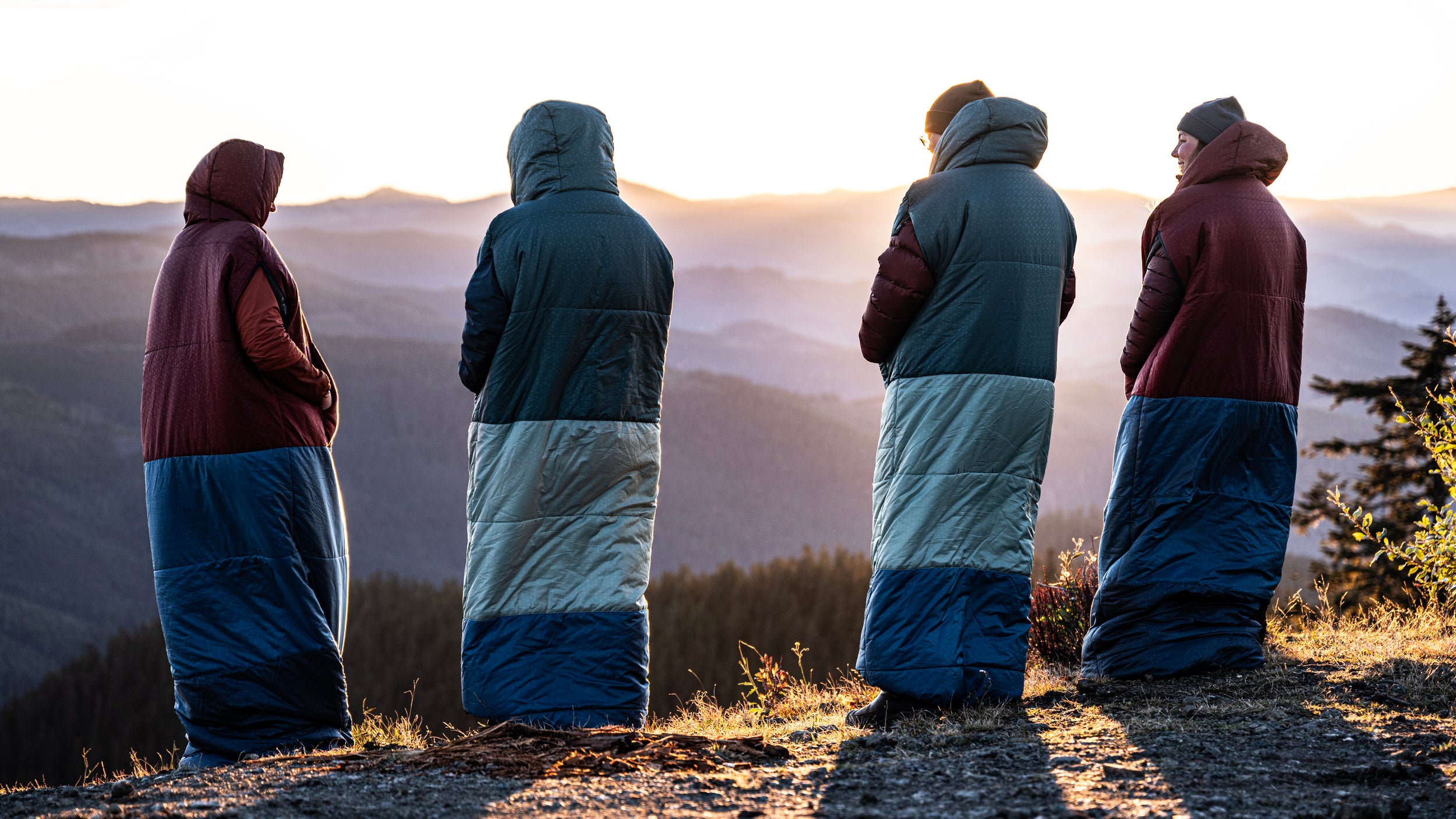 Four campers watch the sunrise while wearing their DreamWalker sleeping bags