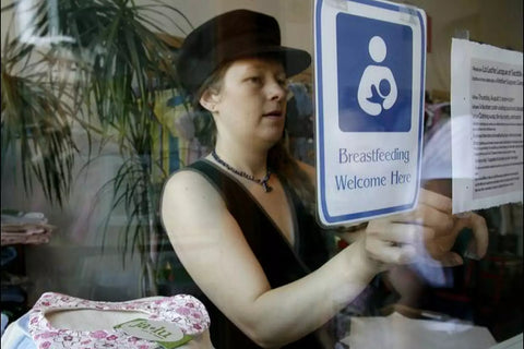 Ellie  in the shop and putting up a sign that says Breastfeeding is welcome here!