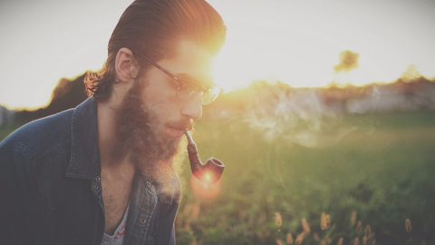 A man with glasses and a beard smoking a pipe
