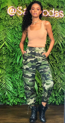 Modelo posando com calça jogger feminina com estampa militar, em frente a um letreiro da SAK Modas.