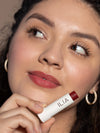 Woman with olive skin wearing ILIA Balmy Tint in Wanderlust, a cool berry lip balm