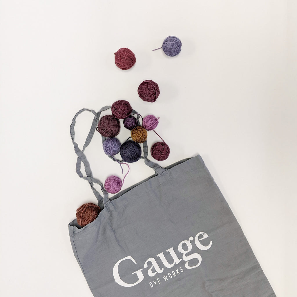 lots of little yarn balls spilling out of a grey Gauge Dye Works tote bag