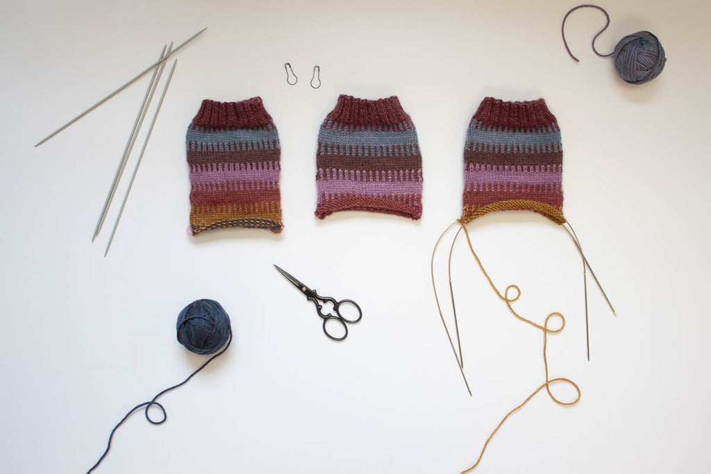 flatlay of three unfinished hand knit socks in a row