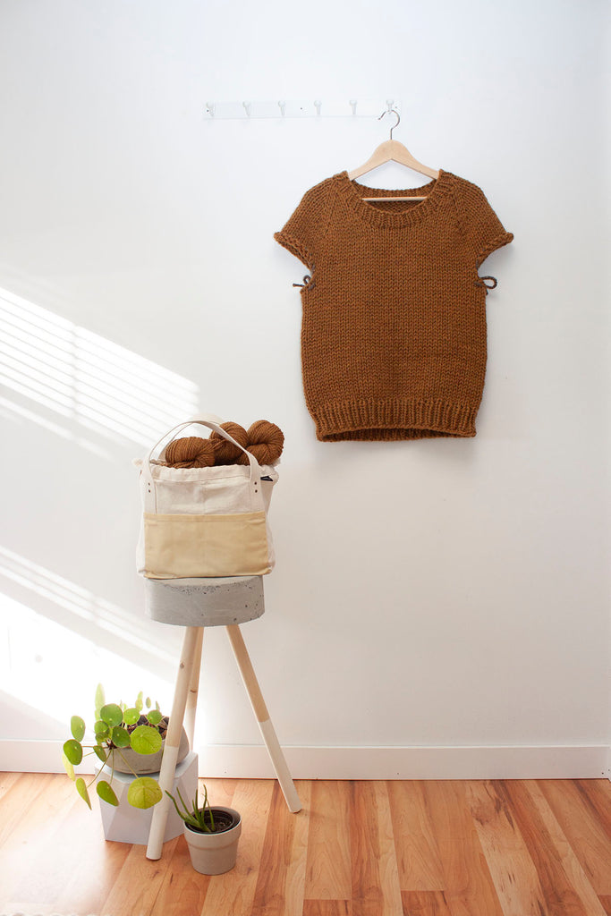 a half finished handknit sweater hangs on a hanger against a white wall