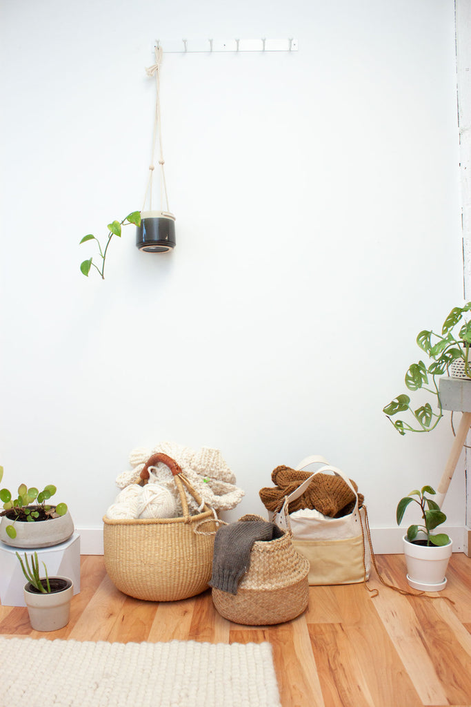 multiple knitting projects in bags and baskets on the floor surrounded by house plants