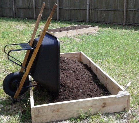 Wheelbarrow tipping forward to unload Overalls Magic Mix into a customer's DIY raised bed garden