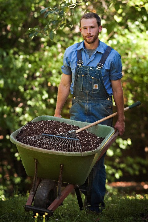 A young @ManInOveralls pushing a wheelbarrow full of Overalls Magic Mix towards a customer's garden to fill their raised beds