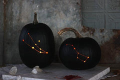 Black pumpkins carved with dots and lines to represent constellations, on a spooky dark background. 