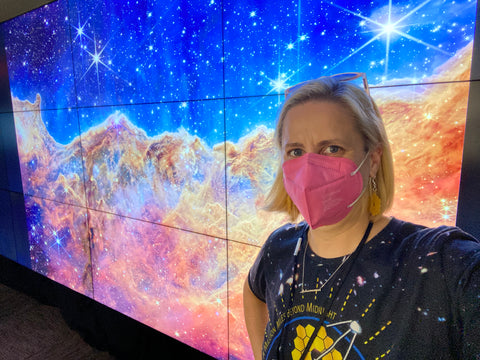 Selfie of Emily with a digital display of the Cosmis Cliffs Carina Nebula JWST image in the background 