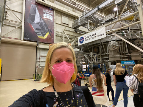 Selfie of Emily in an inegration and testing facility at NASA's Goddard Space Flight Center, with a large poster of NASA's Roman Space Telescope in the background.