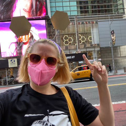 Selfie of Emily wearing sparking gold hexagon bopper headband and pointing to gold hexagons in a shop window in the background