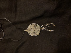 Circular pendant with blue white stones in the center and small strings of stones at the bottom, all on a black cord on a black background.