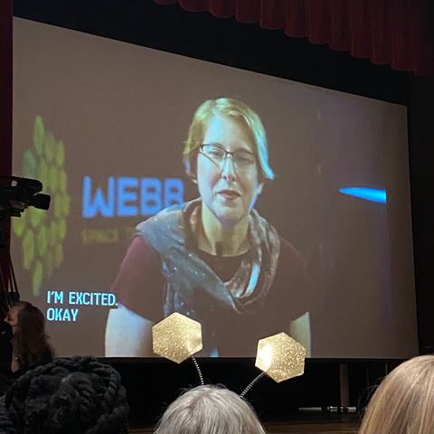 Dr. Jane Rigby on screen at the JWST First Images press conference, with gold glitter hexadon headband boppers in the foreground.