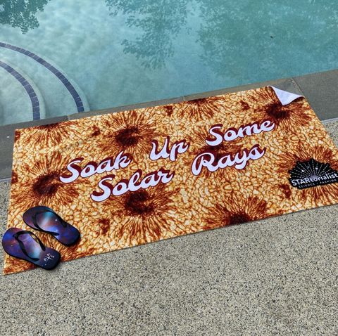 A towel with sunspots sitting next to a pool with flip flops