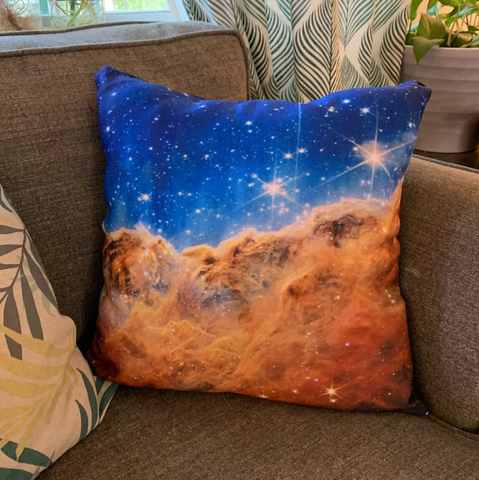 A pillow with an image of the Carina Nebula from JWST on a grey couch