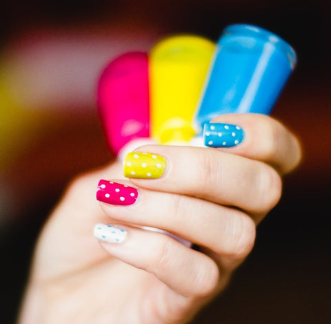 Bandage painted nails in pink, yellow and blue with the same nail polish in hand