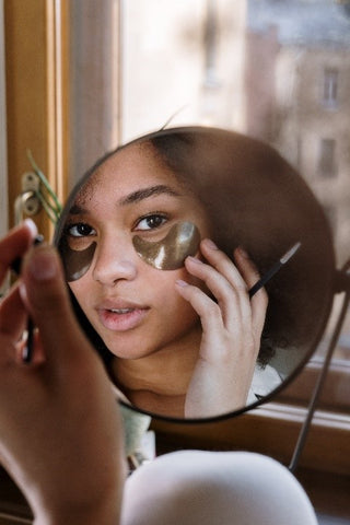 Women looking in mirror putting on gold mask