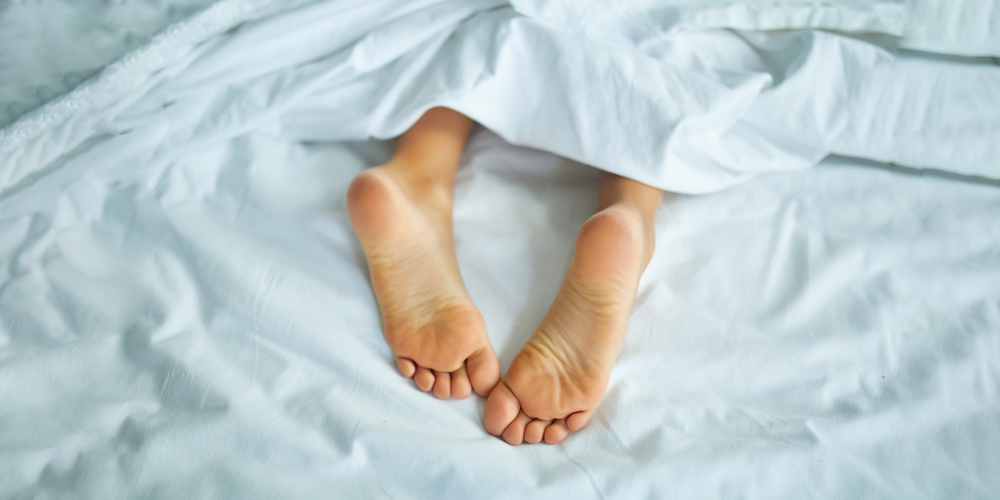Girls' feet covered with white bed sheets