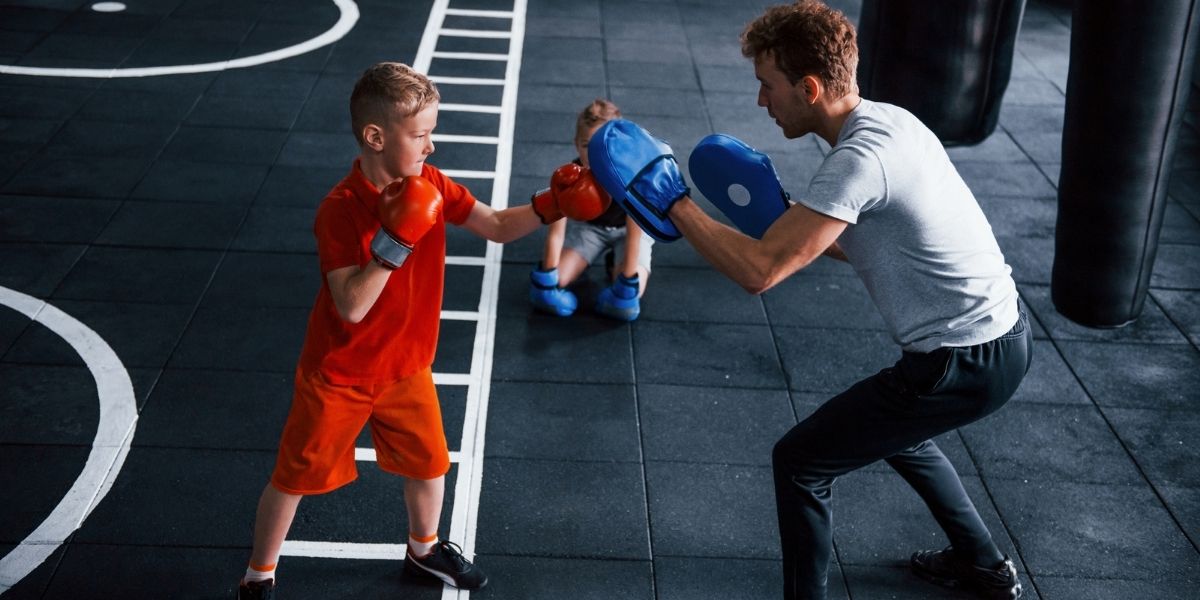 Jeune entraîneur enseigne aux enfants le sport de boxe dans la salle de gym