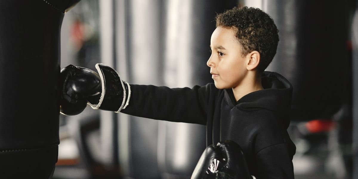 Petit garçon en gants de boxe sur un ring frappant un sac de frappe