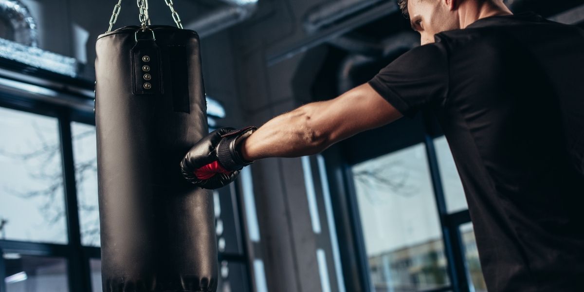 vue de côté d'un beau boxeur s'entraînant avec un sac de frappe dans un gymnase