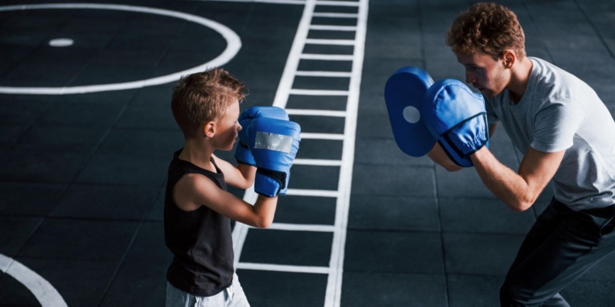 Jeune entraîneur enseigne le sport de boxe enfant dans la salle de gym