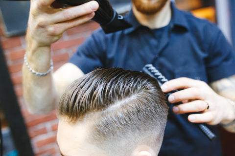 A barber cutting and styling a side part hairstyle