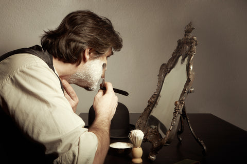 Мужчина использует опасную бритву дома перед зеркалом