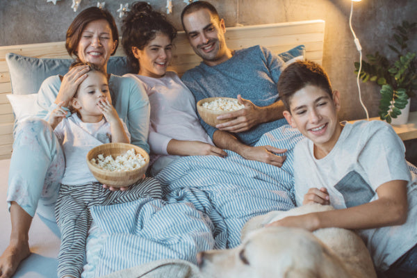 10 ways to relax and recharge this holiday season family in bed watching a movie with popcorn happy relaxed