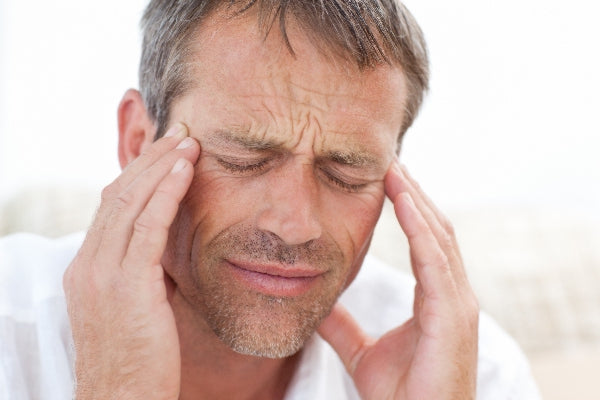 11 Warning Signs of Magnesium Deficiency man wearing white shirt rubbing temples with a headache