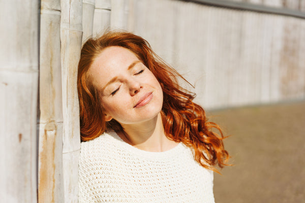 young woman soaking up the sun against a fence