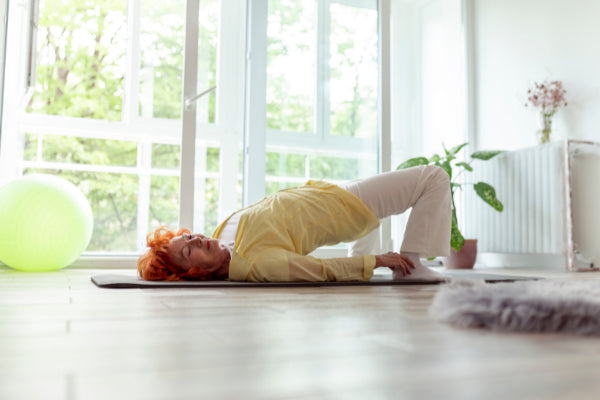 4 exercises for back pain relief senior woman doing bridge stretch to relieve back pain in bright living room