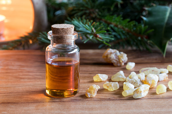 A bottle of frankincense oil next to frankincense cubes on a table