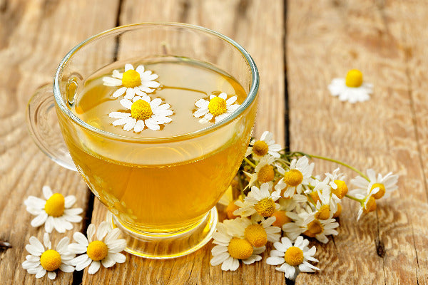 9 chamomile benefits chamomile essential oil benefits backed by science chamomile tea and flowers on a wood table