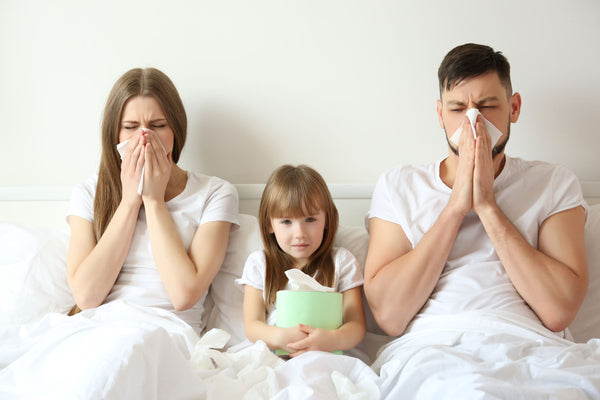 Mom and dad sitting in bed with their kid blowing their nose