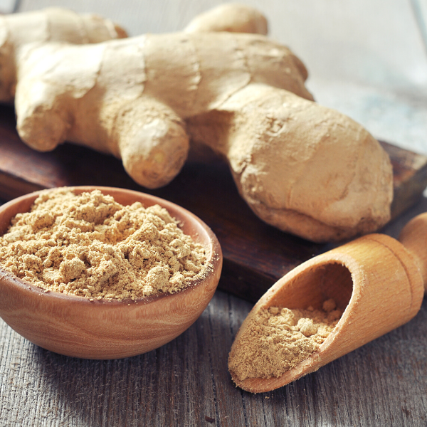 Freshly ground ginger root in a wooden bowl with scoop next to cutting board