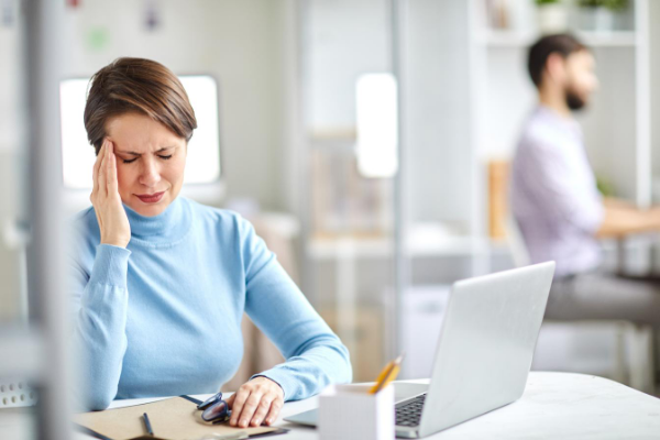 Woman in blue shirt having migraine at desk while working 