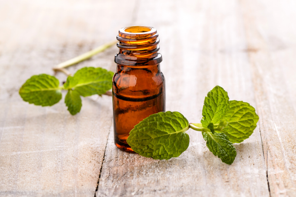 Peppermint leaves next to amber glass bottle with essential oils