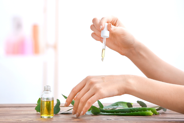 Woman applying essential oil drops to hand with aloe leaves