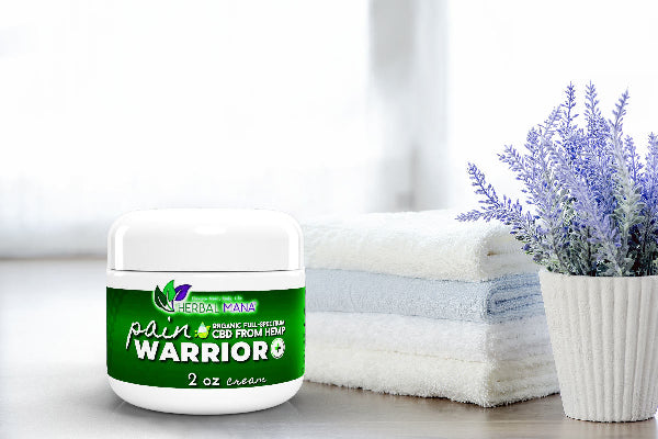 Pain Warrior+ Cream On wood table next to towels and lavender plant
