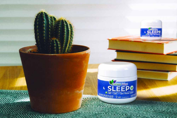 Sleep+ CBD Infused DMSO cream sitting on table next to cactus and on stack of books