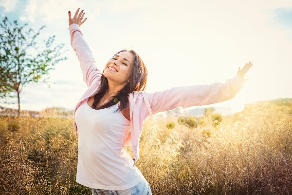 What are the Health Benefits of Vitamin B12 girl in a field under the sun smiling arms above her head happy