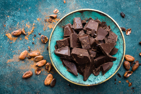 foods that boost your mood yes please chocolate in a blue bowl with cocoa beans scattered around close up