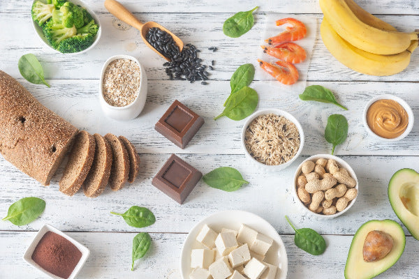 how to correct magnesium deficiency foods with magnesium banana shrimp black beans pumpkin seeds avocado peanuts peanut butter dark chocolate whole grains broccoli on a white rustic wooden table