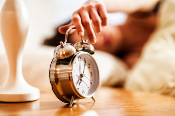 how to stick to a killer morning routine person reaching for their alarm clock from the bed close up