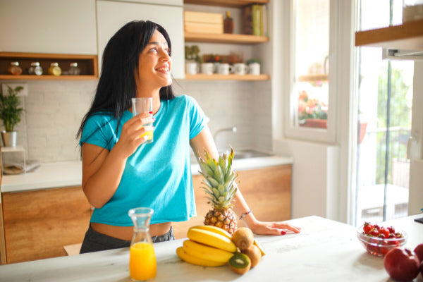 how to stick to a killer morning routine woman at kitchen counter drinking orange juice smiling in the morning